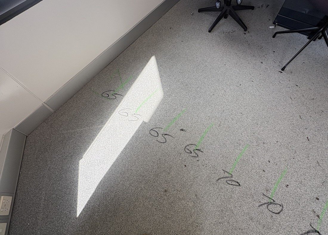 Carpet tiled office floor with green tendon marks at regular intervals, each with the recorded cover in millimetres written alongside, reading 65 and 70.