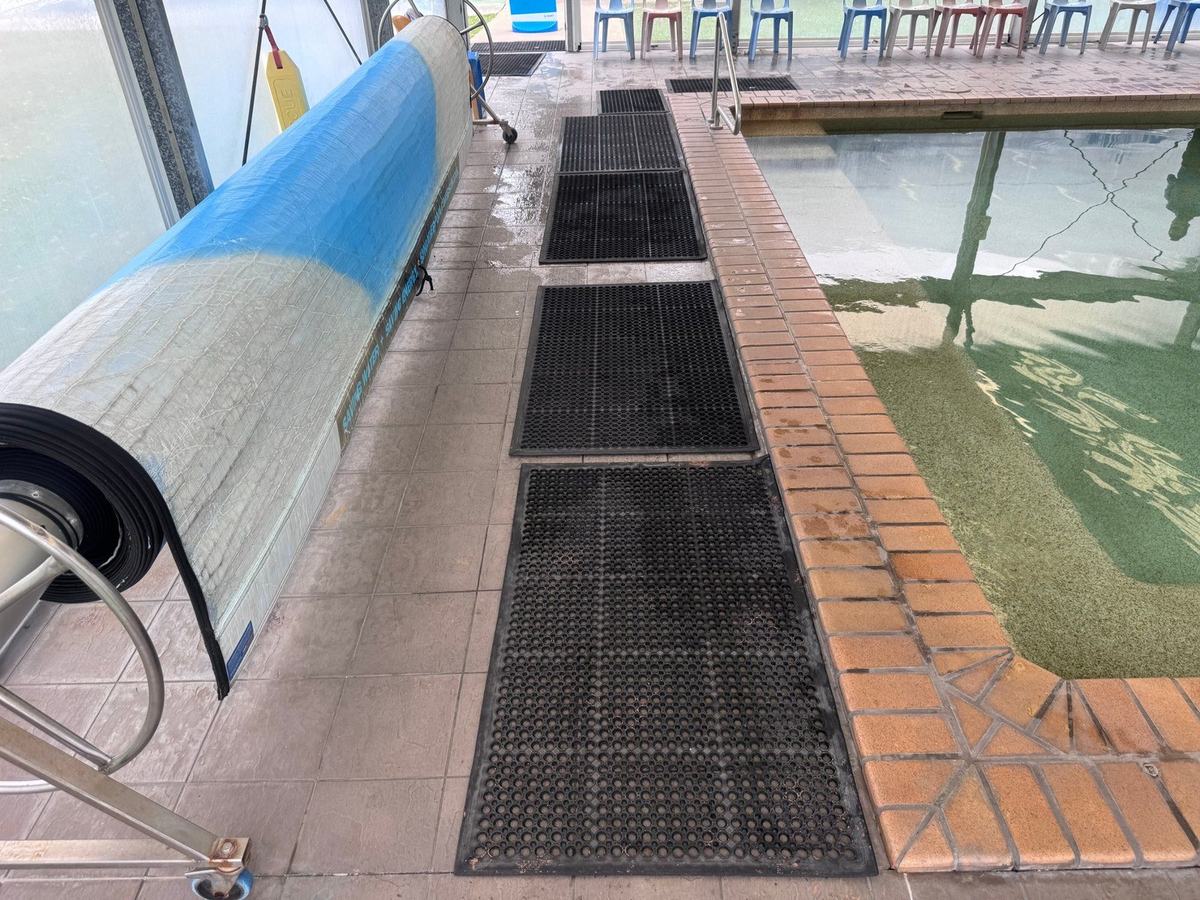 Wet tiled pool deck with rubber matting beside the pool cover roller